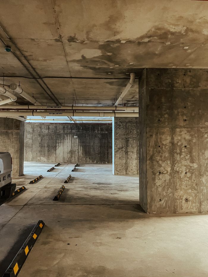 A vacant indoor concrete underground parking garage with minimal vehicles and structural columns.