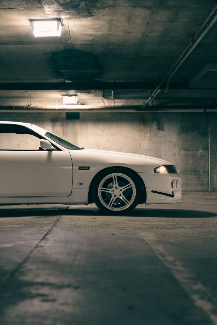 Retro white car parked in a dimly lit urban garage, showcasing its classic design and vintage appeal.