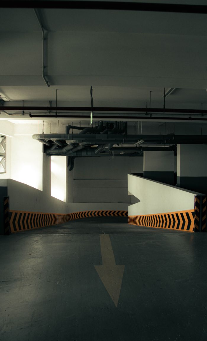 A shadowy interior view of a concrete parking ramp with directional arrows and industrial lighting.