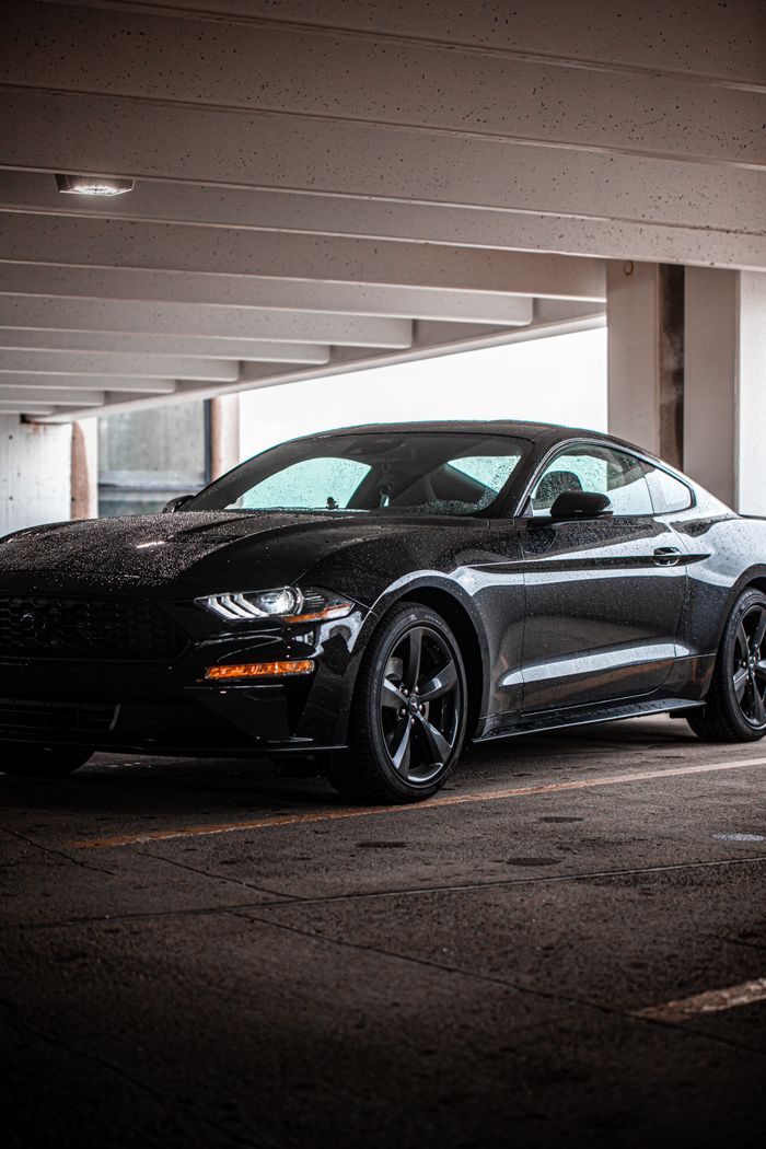 A stylish black Mustang sits parked in a dimly lit urban parking garage, showcasing its sleek design.