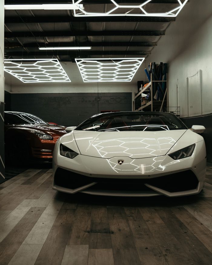 Front view of a luxurious white Lamborghini inside a modern garage with geometric lighting.